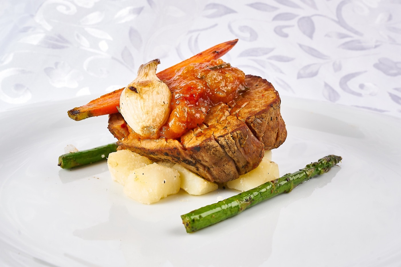 Filete de res con compota de tomate rostizado acompañado de papa rostizada espárragos y cebolla cambray caramelizada.